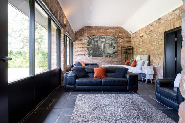 Luxury Lakeview Retreat: Open-plan living area with leather sofas, brick walls and the bed beyond